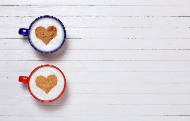 Two cups of coffee with heart shape symbol on wooden white background