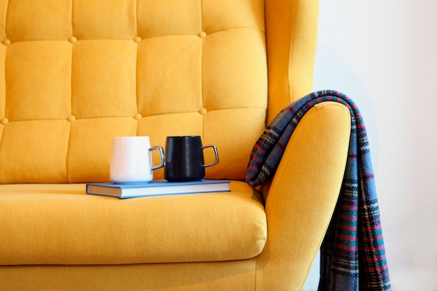 two cups of tea and blue book on a yellow coach with blanket still life details in home interior