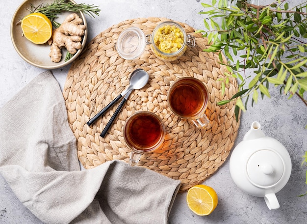 Two cups of tea with lemon ginger teapot and dry herbal flowers on a marble background in the early morning Healthy breakfast concept Top view