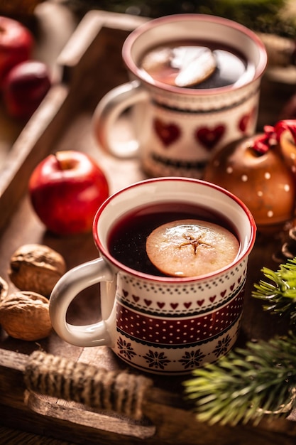 Two cups with Christmas hot punch cooked from red wine rum and fresh fruit flavored with cloves and cinnamon