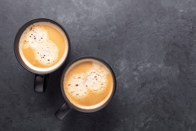 Two cups with coffee on dark stone.