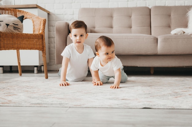 Photo two cute babies in white tshirts crawl and play on the floor of the house two brothers