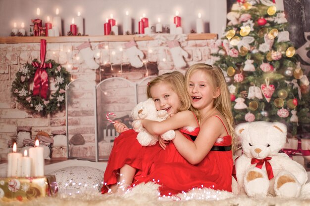 Two cute cheerful girls in Christmas clothes against the background of the Christmas tree