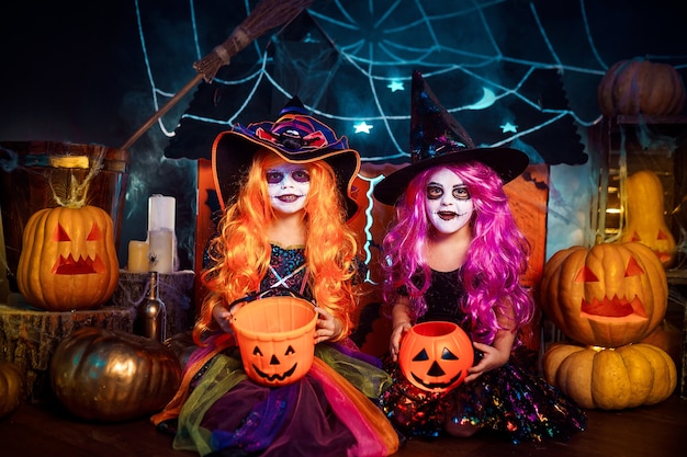 Two cute funny sisters celebrate the holiday. Jolly children in carnival costumes ready for Halloween in halloween decorations