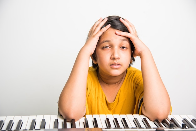 Two Cute little Indian or Asian girls playing piano or keyboard, a musical instrument, over white background