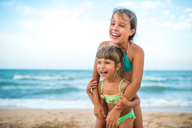 Two cute positive little girls sisters raised their hands up while swimming at sea during the holidays on a warm summer day. Concept of healthy and joyful children