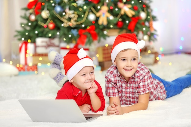 Two cute small brothers using laptop on Christmas decoration surface