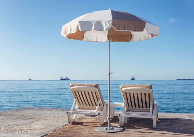 Two deckchairs under a parasol near the calm sea