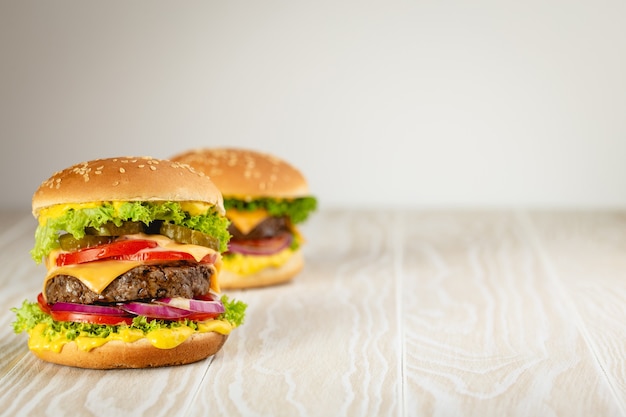 Two delicious burgers with meat, melted cheese, dripping sauce and vegetables on white wooden rustic background with space for text. Freshly made tasty hamburgers, close-up and copy space