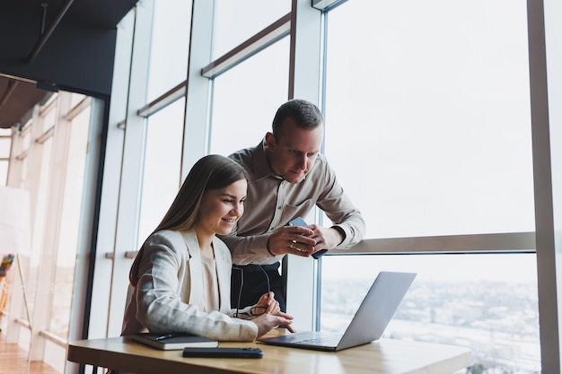 Two different businessmen talking and working together on a new project on a laptop while sitting in a large modern office