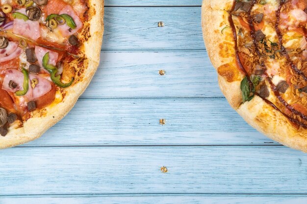 Two different delicious big pizzas on a blue wooden background