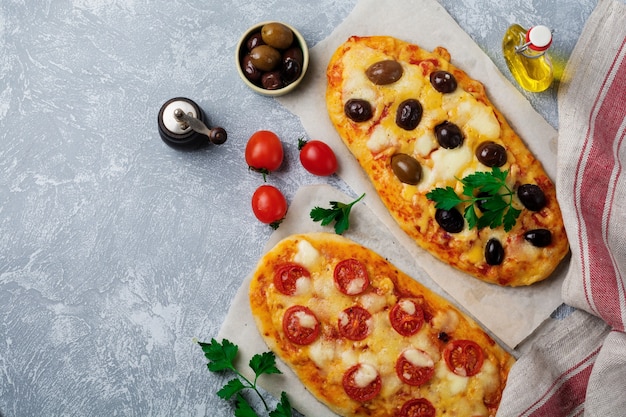 Two different oval Greek pizza with olives and tomato Margarita on gray concrete.   