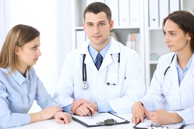 Two doctors  and  patient sitting at the table in medical cabinet.  High level and quality medical service concept.