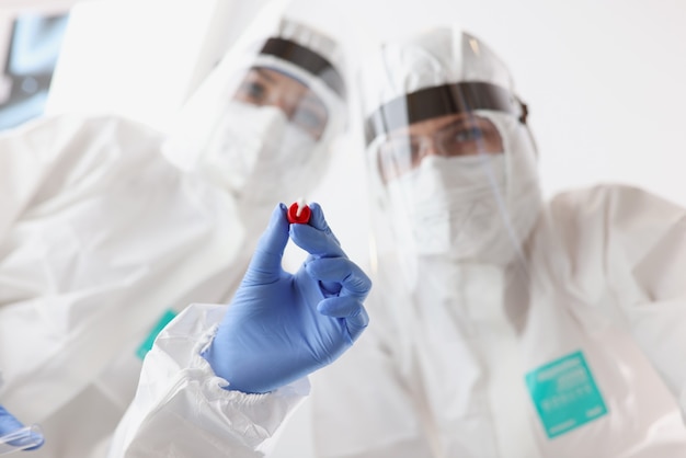 Two doctors in protective suits and goggles are holding shelf and test tube for taking biological ma...