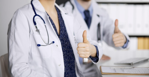 Photo two doctors sitting with thumbs up in hospital office. medical help, countering viral infection and medicine concept.