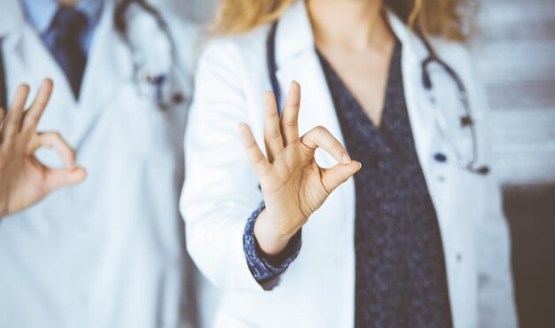 Two doctors standing with Ok sign in hospital office. Medical help, countering viral infection and medicine concept.