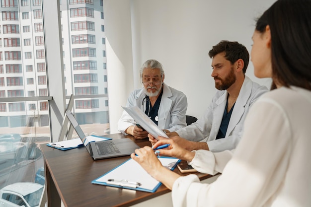 Two doctors in white uniform consult female patient at meeting in private clinic