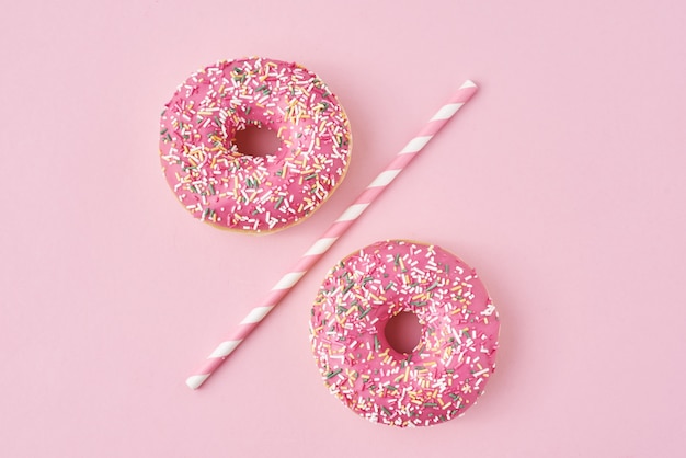 Two donuts separated with drinking straw on pink surface. Creative food concept