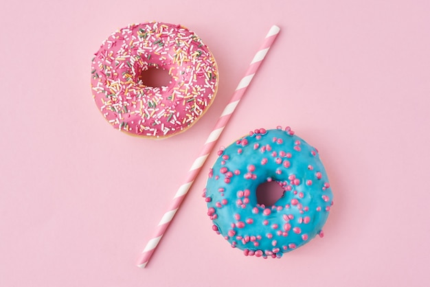 Two donuts separated with drinking straw on pink.