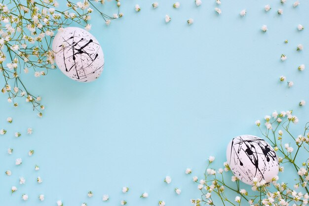 The two eggs are white in color with black spots and flowers on a blue background with a copy of the space. Easter. Minimalism. Festive background. Postcard. Frame