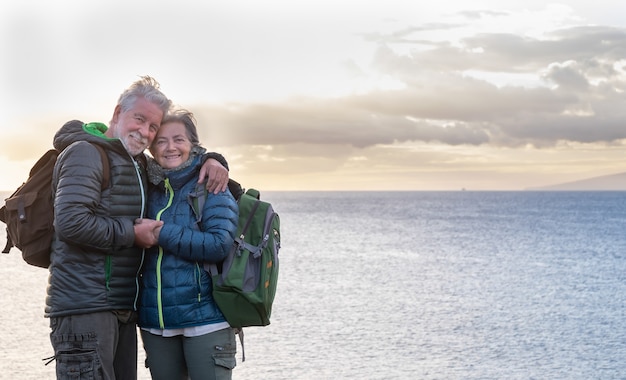 Two elderly people hug each other in front of sea enjoying the sunset light Standing on the cliff