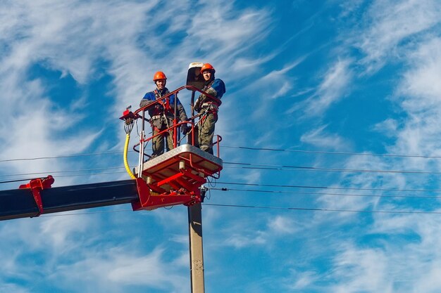 Two electricians from the cradle of an aerial platform or crane are repairing a street lighting