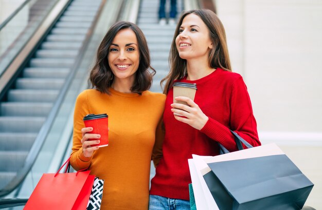 Two elegant and stylish beautiful young women with shopping bags are walking in the mall while black friday sale