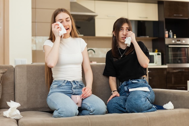 Two emotional girlfriends watching a melodrama on TV and crying while sitting on the sofa