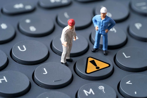 Two engineer miniature figure standing to analysis with yellow exclamation caution warning mark sign on computer keyboard for notification error and network maintenance concept