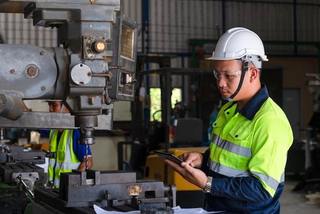 Two engineer team workers or professional foreman in hard hat using blueprints on digital tablet while standing at industrial plant teamwork concept