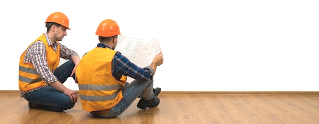 The two engineers with a paper sit on the floor on the white wall background