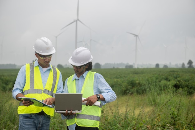 Two engineers working and holding the report at wind turbine farm Power Generator Station on mountainThailand people