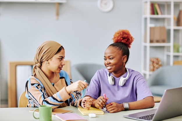 Two ethnic young women chatting in workplace setting and smiling