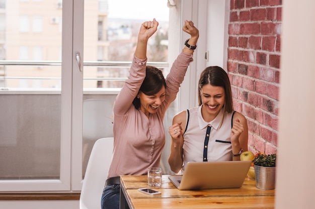 Two excited roommates reading good news on line with a laptop 