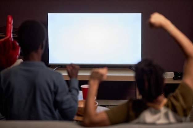 Two excited sports fans watching match on TV with blank screen mockup