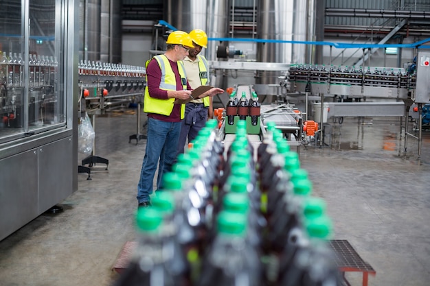 Two factory workers monitoring cold drink bottles on production line