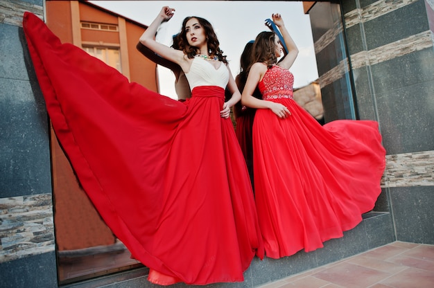 Two fashionable girls at red evening blowing dress in the air 