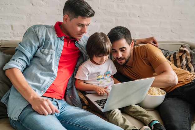 Two fathers enjoy wathching movies with their son at home.