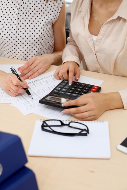 Two female accountants counting on calculator income for tax form completion hands closeup. Internal Revenue Service inspector checking financial document. Planning budget, audit  concept