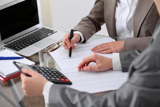 Two female accountants counting on calculator income for tax form completion hands closeup. Internal Revenue Service inspector checking financial document. Planning budget, audit  concept