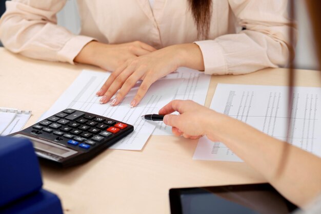 Two female accountants counting on calculator income for tax form completion hands closeup. Internal Revenue Service inspector checking financial document. Planning budget, audit  concept