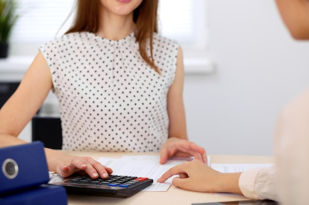 Two female accountants counting on calculator income for tax form completion hands closeup. Internal Revenue Service inspector checking financial document. Planning budget, audit  concept