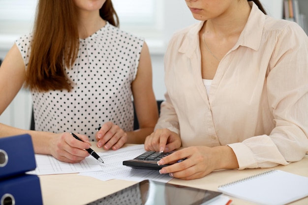 Two female accountants counting on calculator income for tax form completion hands closeup. Internal Revenue Service inspector checking financial document. Planning budget, audit  concept