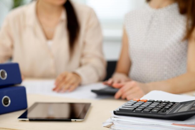 Two female accountants counting on calculator income for tax form completion hands closeup. Internal Revenue Service inspector checking financial document. Planning budget, audit  concept