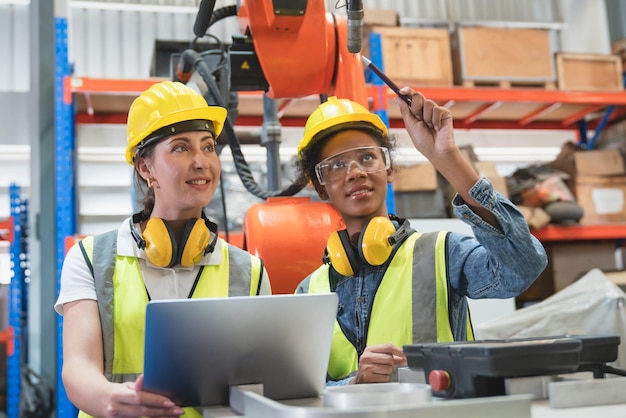 Two female automation engineers inspection head welding robot arm machine with laptop in factory