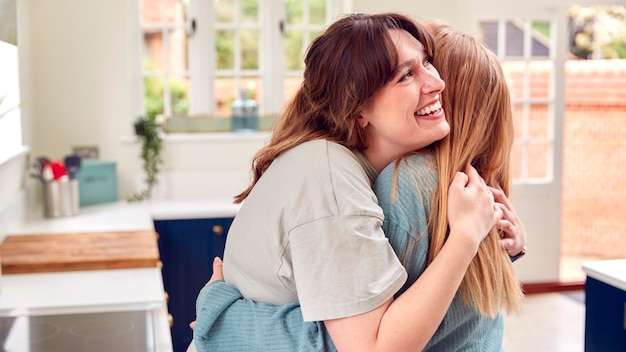 Two Female Friends Greeting And Hugging In Kitchen At Home