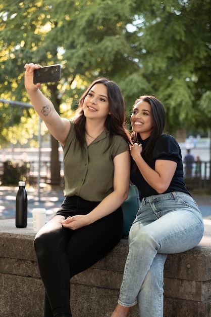 Two female friends taking selfie in the park while having some coffee