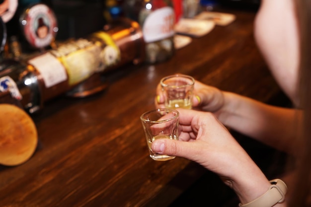 Two female hands clink glasses with alcoholic shots Blurred bar background