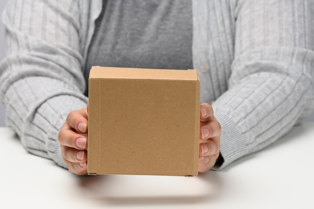 Two female hands hold a square box made of brown corrugated cardboard on a white background, close up