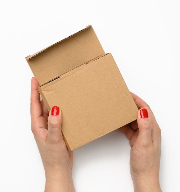 Two female hands hold a square box made of brown corrugated cardboard on a white background